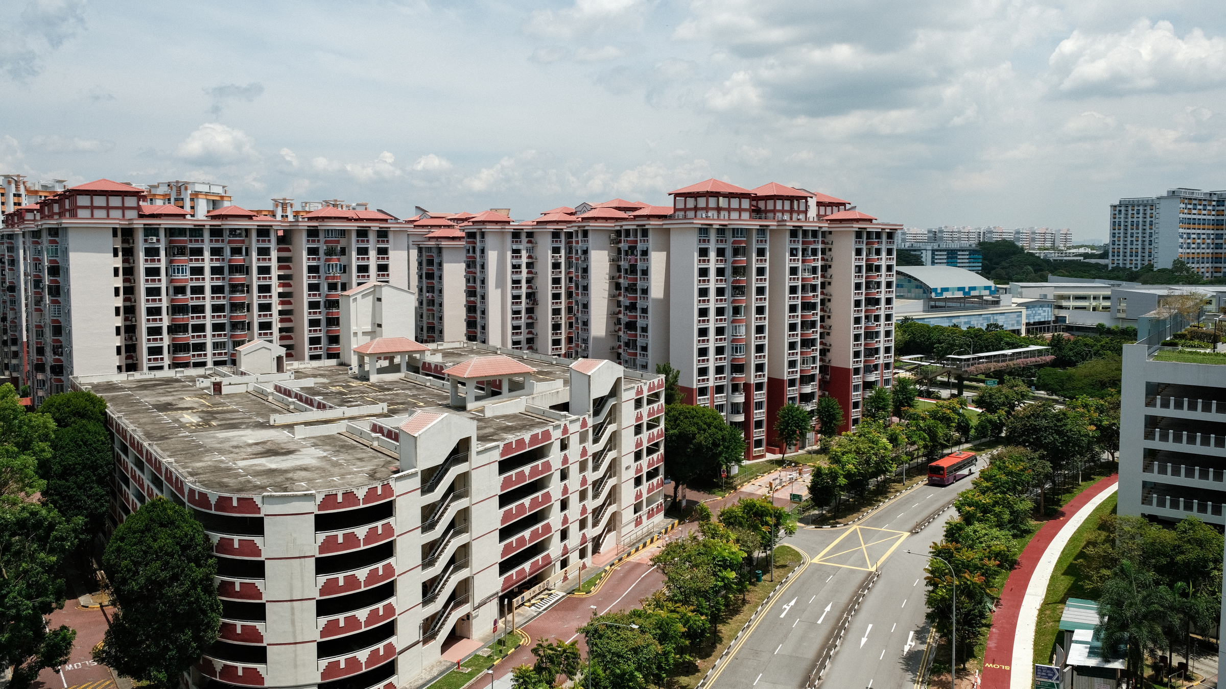 Elevated view of red-roofed HDB blocks and a multi-storey carpark in Jurong West Central under a bright cloudy sky