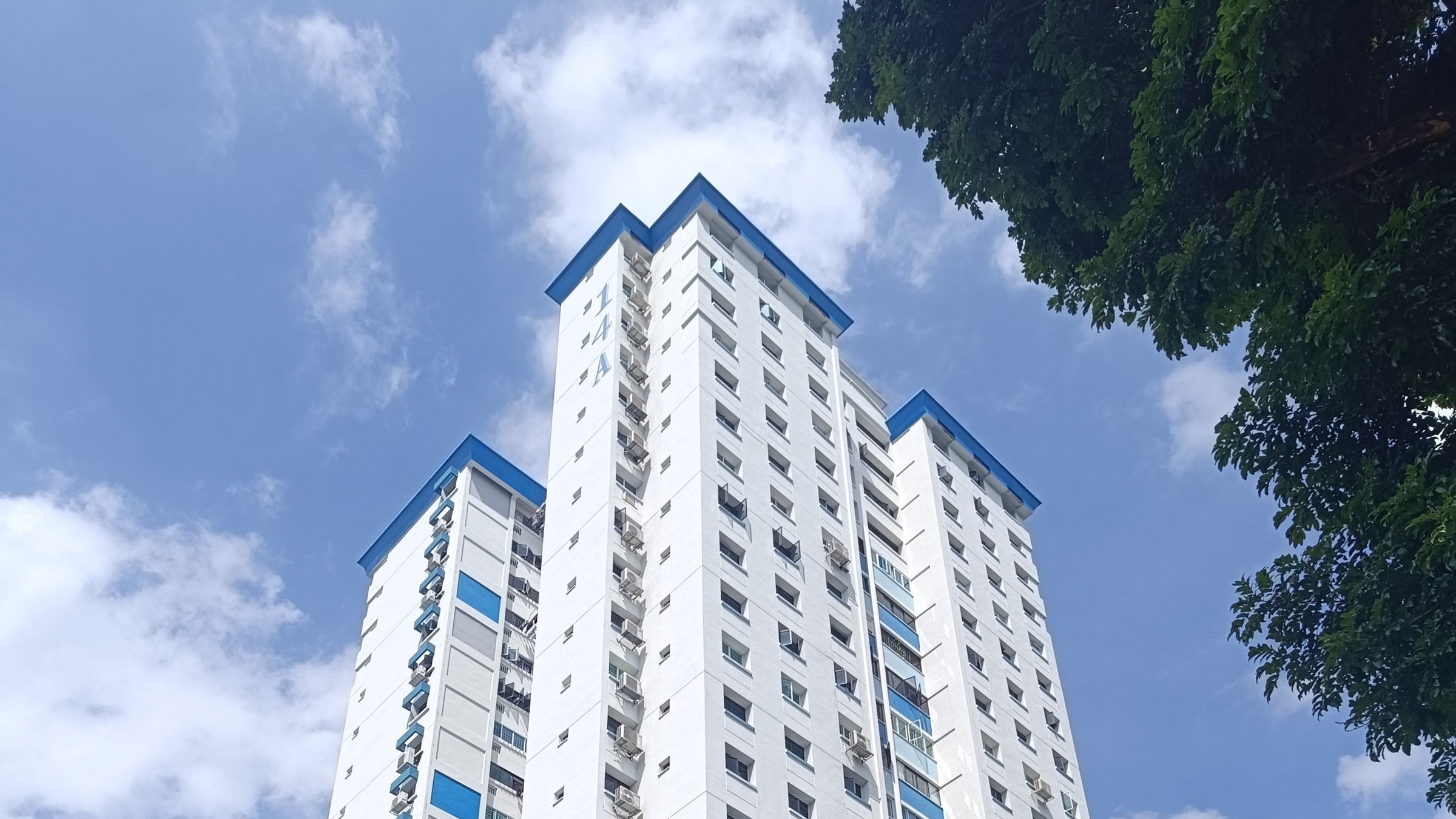 A tall white HDB block with blue trim at Lorong 7 Toa Payoh, seen from below against a blue sky.