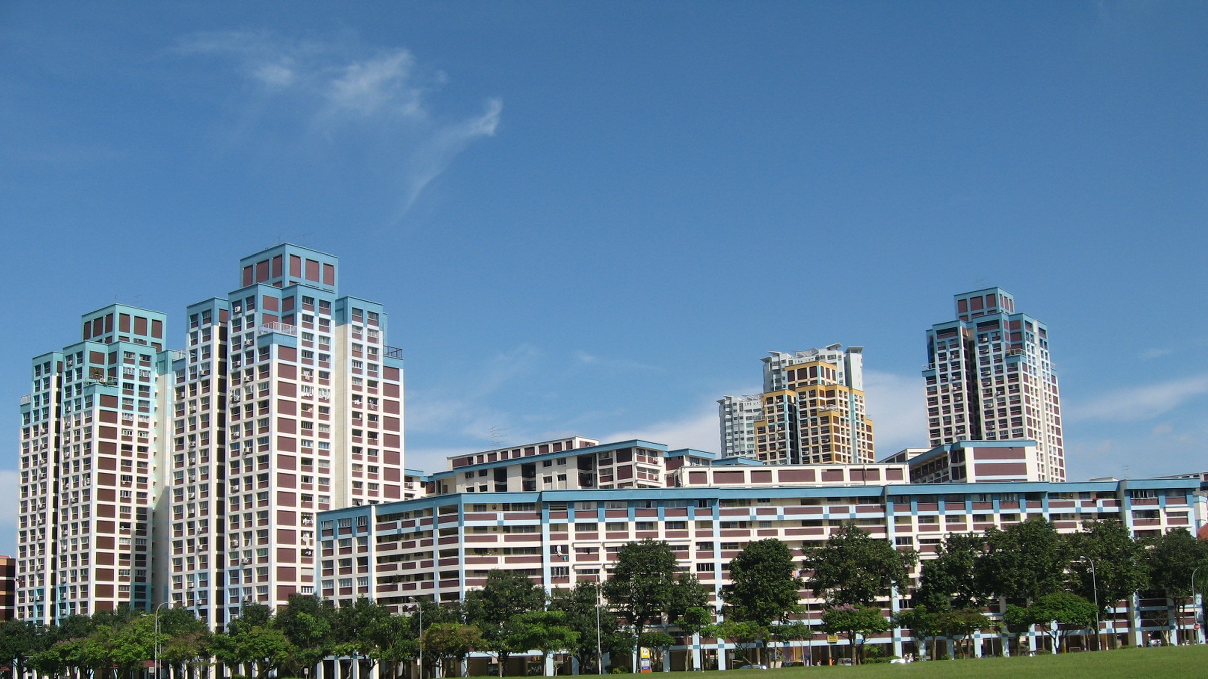 Tall maroon and white HDB point blocks in Bishan rising above a long slab block, seen across an open green field under a blue sky.