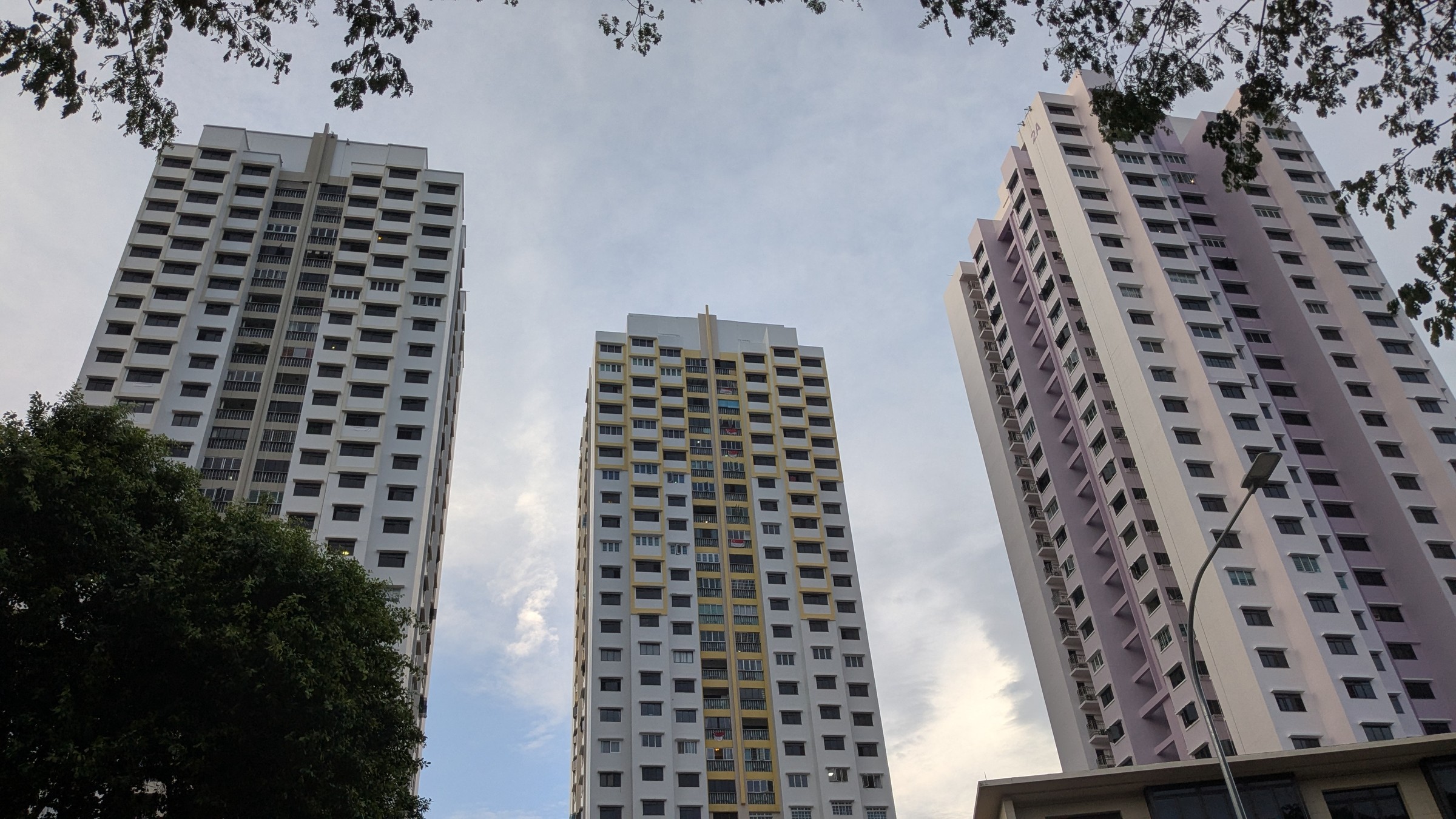 Three HDB tower blocks along Boon Tiong Road in different colour schemes, seen from street level against a partly cloudy sky.