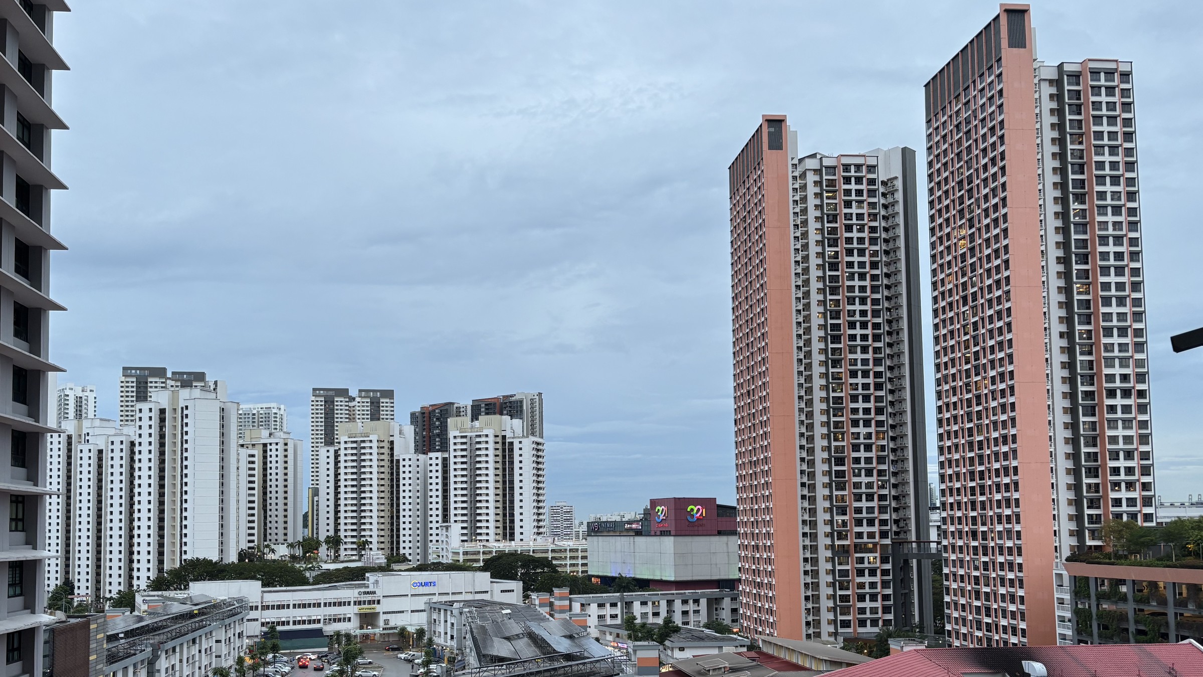 Daytime view over Clementi Central, with older white slab HDB blocks in the middle distance and three modern 40-storey salmon-coloured HDB towers on the right.