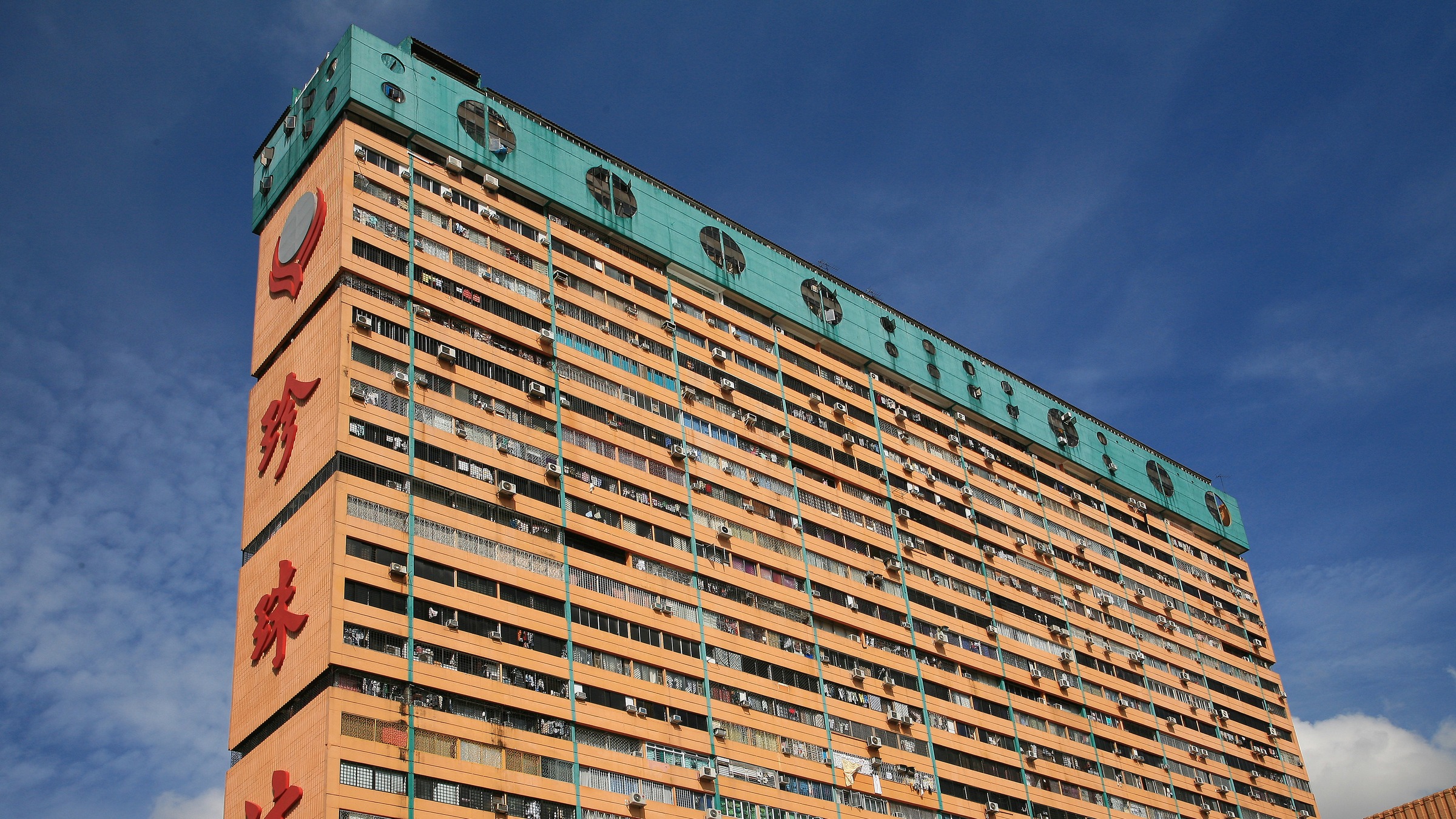 The orange residential tower of People's Park Complex in Chinatown against a blue sky, with its green rooftop crown and Chinese signage.