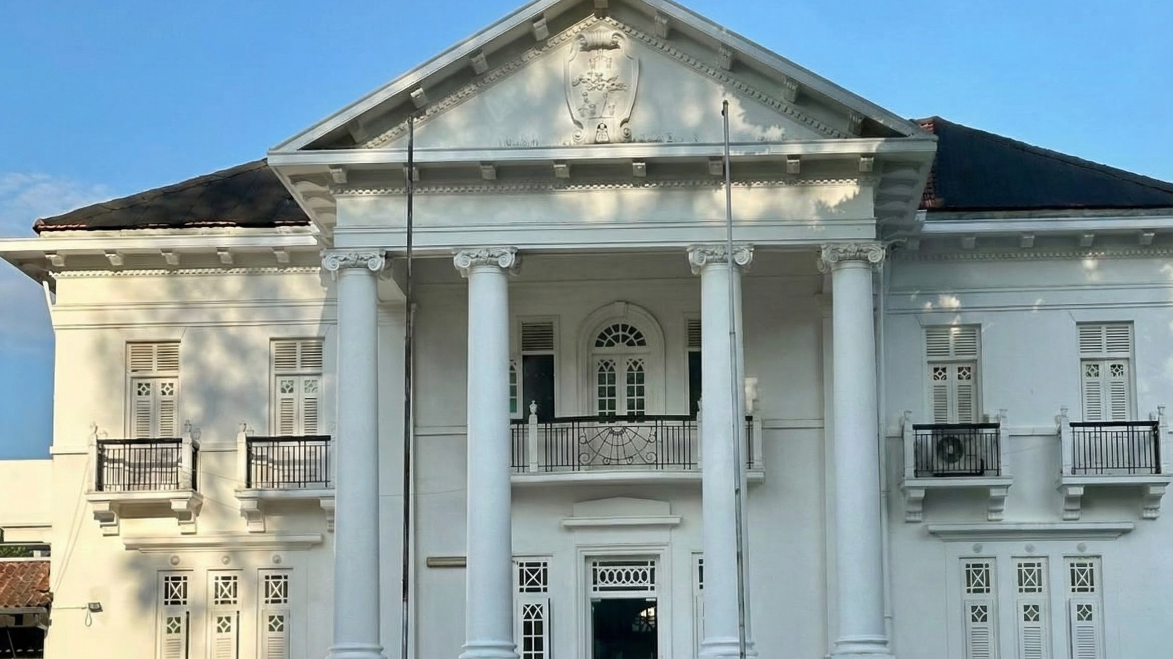 The white colonial-style front facade of Westbourne Mansion at 25 Gilstead Road, Singapore, with columns and a triangular pediment under a blue sky.