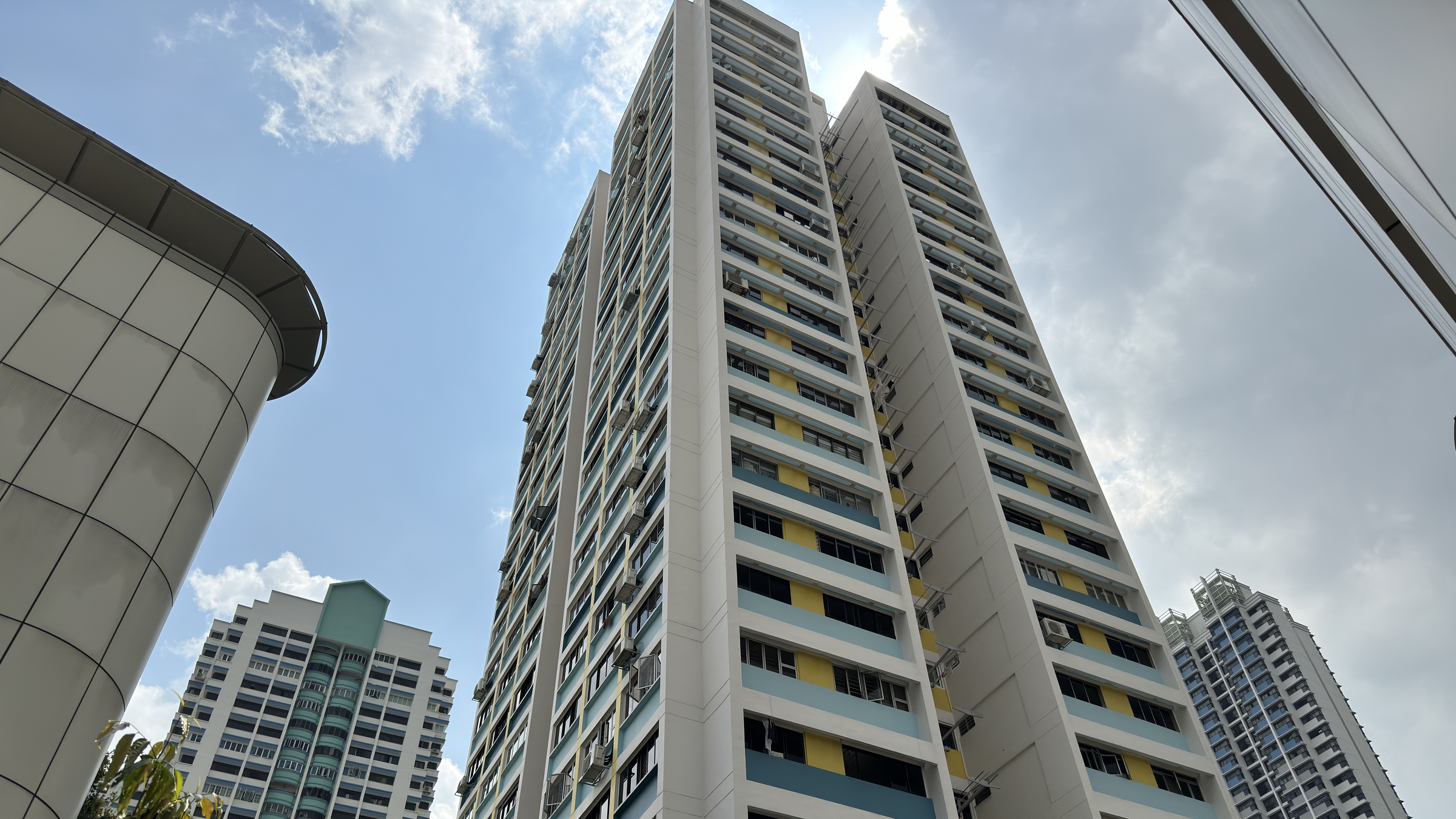 Upward view of HDB residential blocks in Toa Payoh with blue and yellow banded facades against a bright sky
