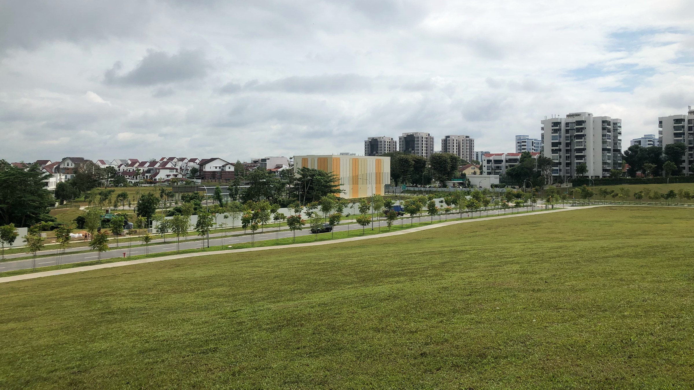 Open cleared land around the Lentor MRT station entrance in December 2021, with landed houses and older condominiums in the distance.