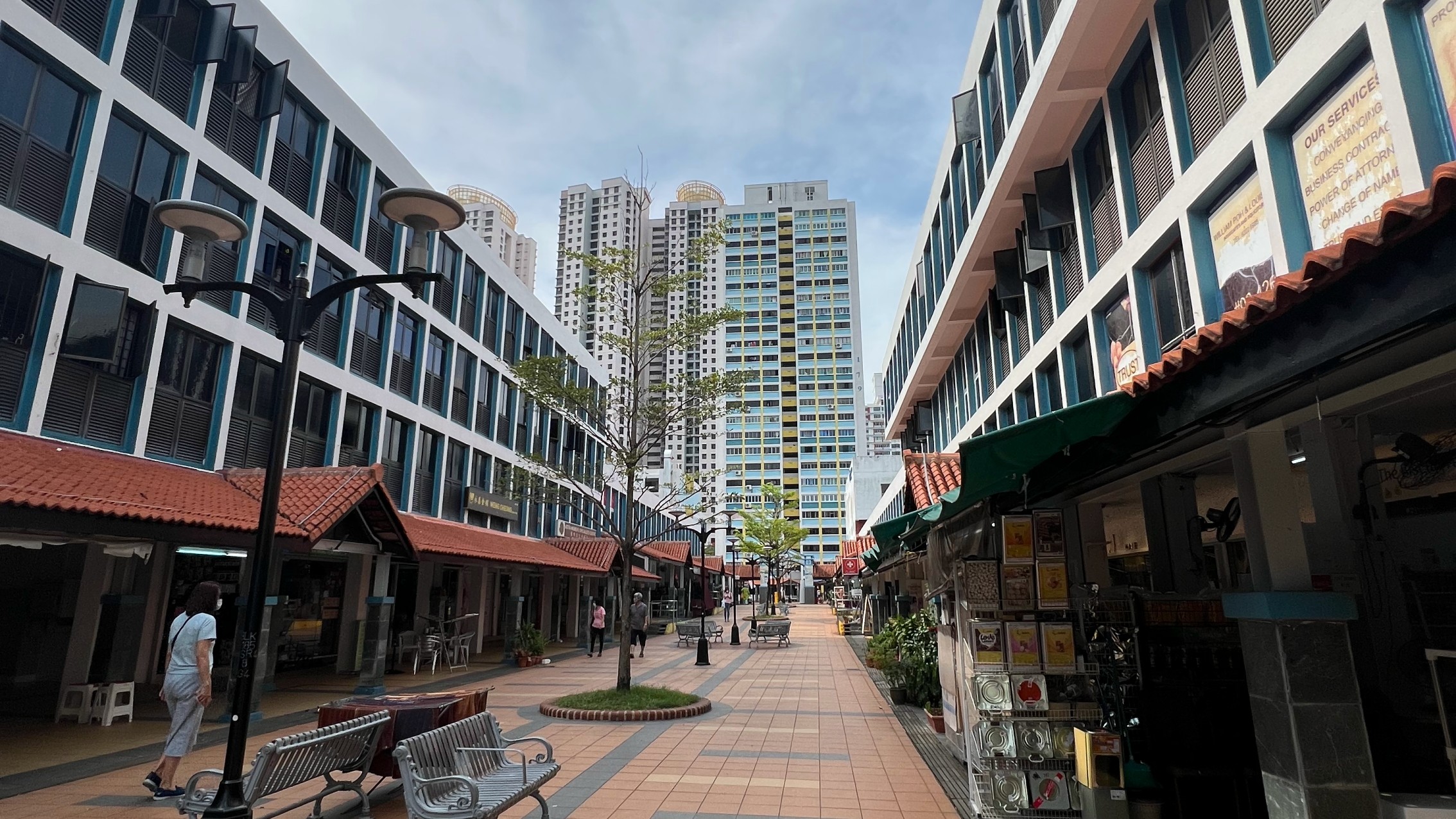 Low-rise shop blocks with red-tiled canopies lining the pedestrian mall at Toa Payoh Central, with an HDB tower rising behind.