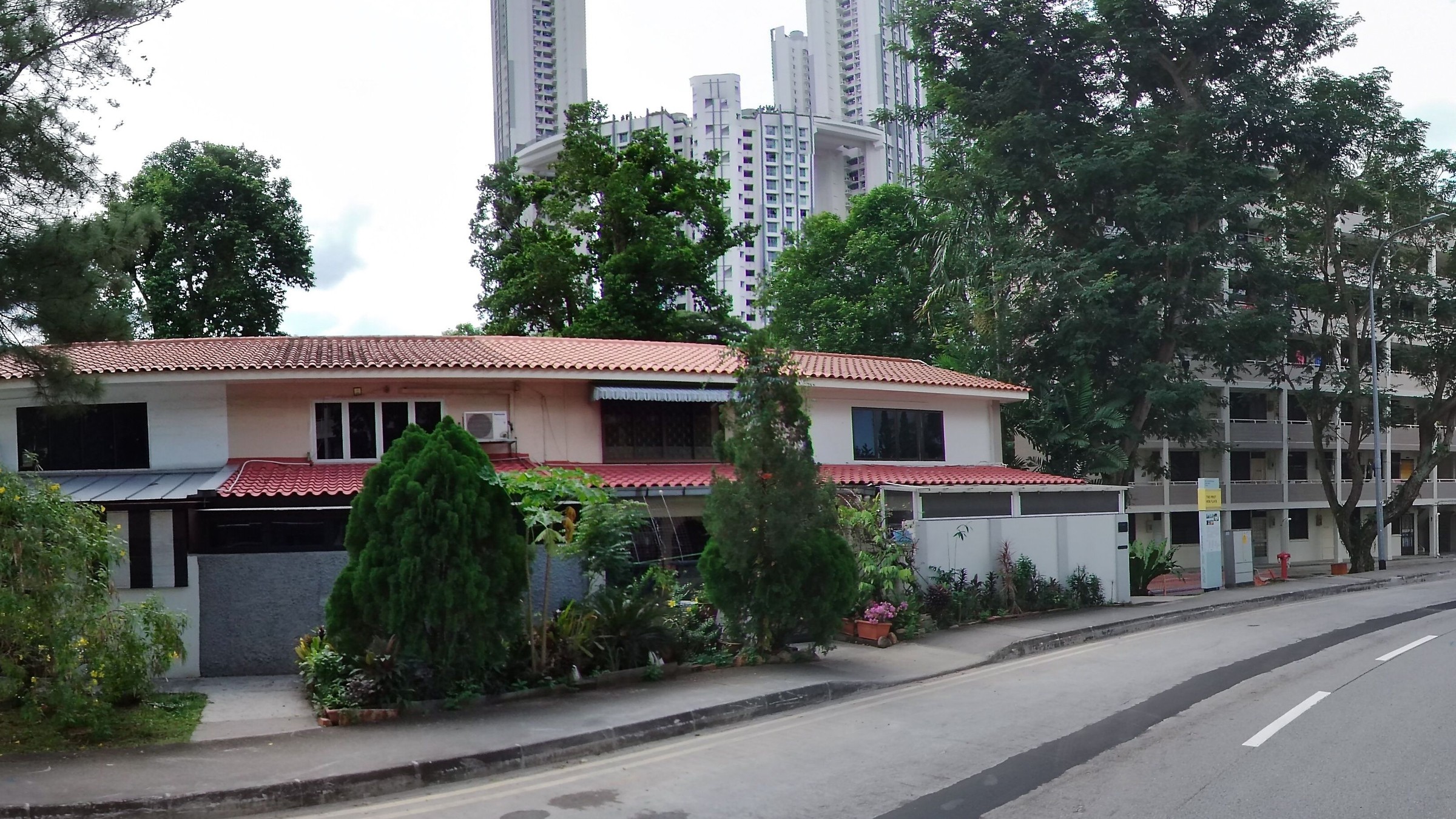 Two-storey terrace houses with red-tiled roofs and lush front gardens along Stirling Road in Queenstown, with tall modern HDB towers rising directly behind them.
